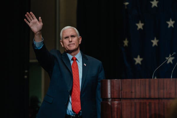 Former Vice President Mike Pence waving, while wearing a suit with a blue shirt and red tie. 