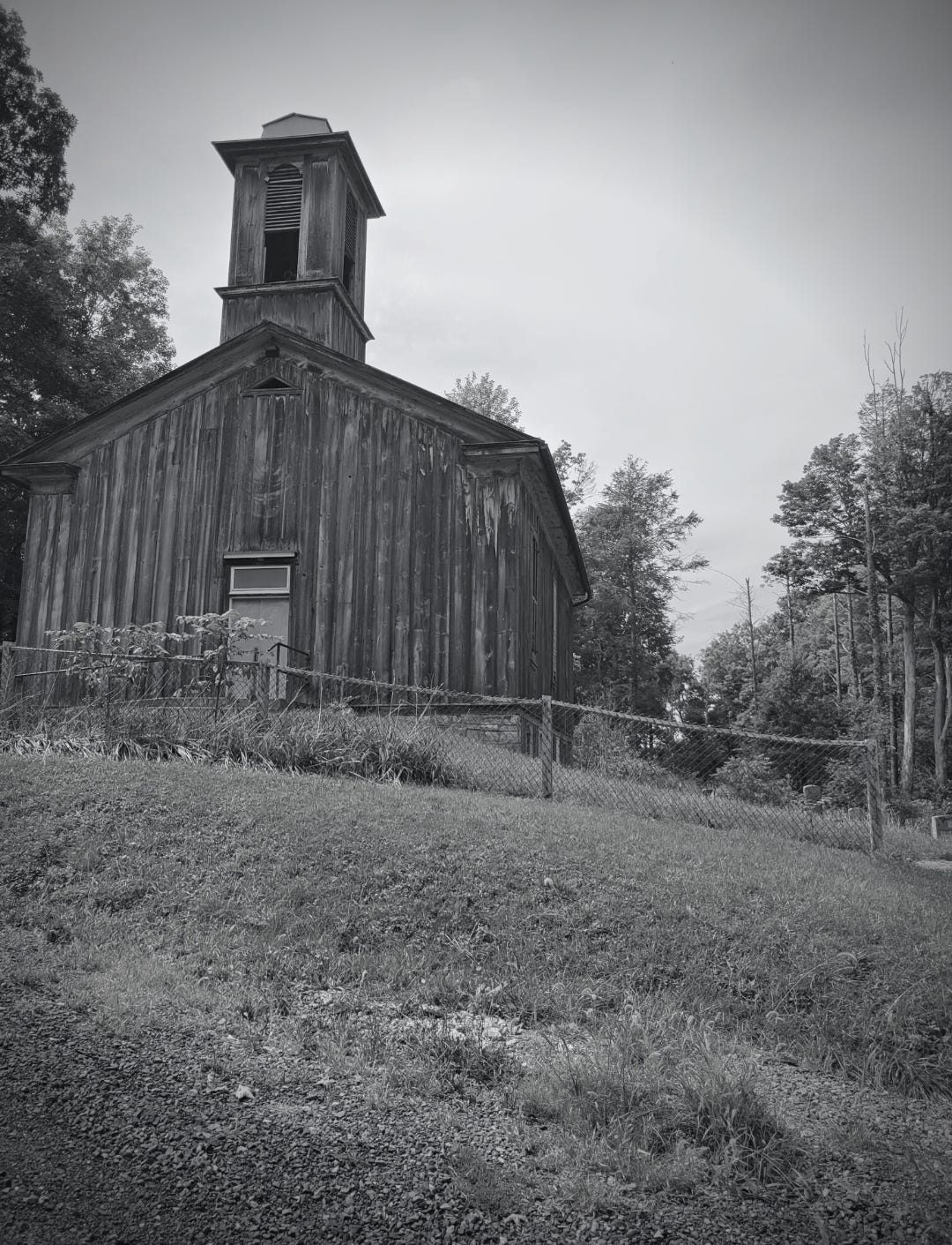 Black and white photo of a rundown church surrounded by trees.