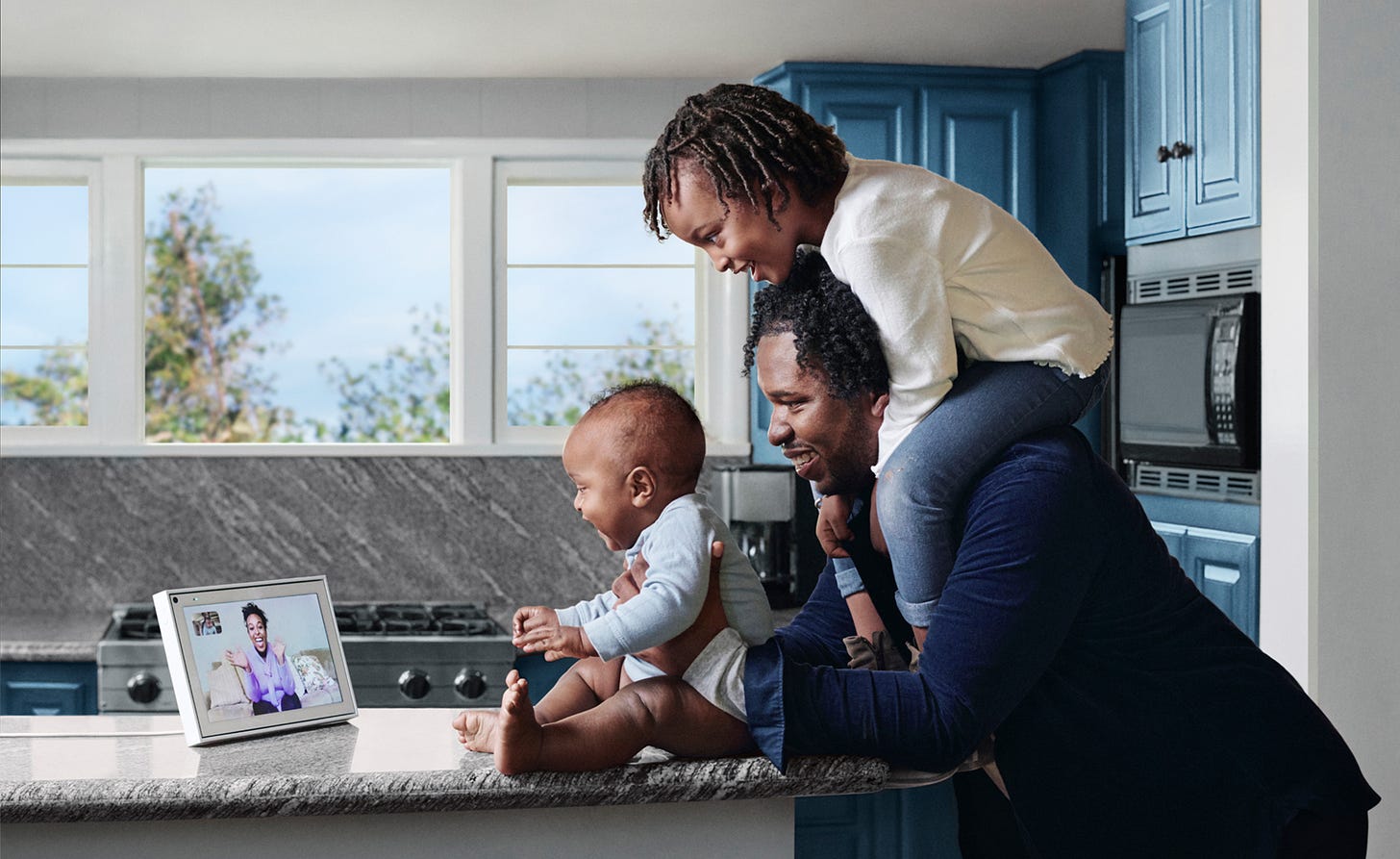 father with two children in kitchen conversing with grandmother via Portal device