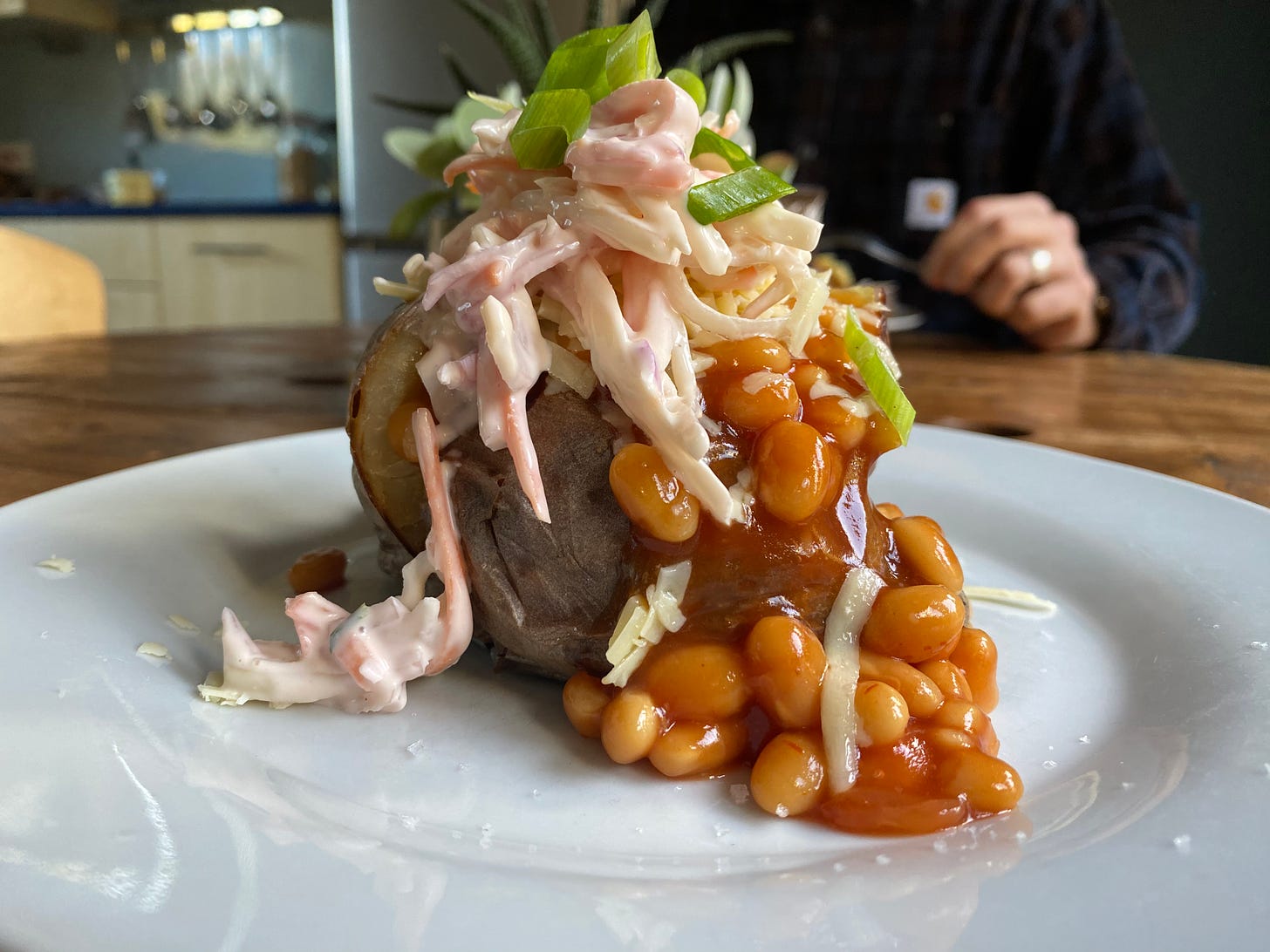 Jacket potato with beans, coleslaw and spring onion on a white plate. 