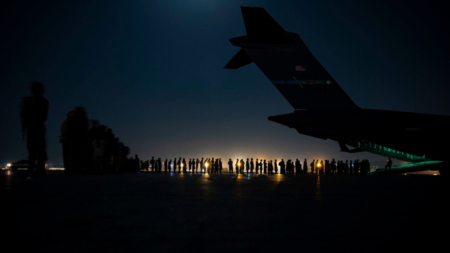 People wait in line to board a military aircraft at night.