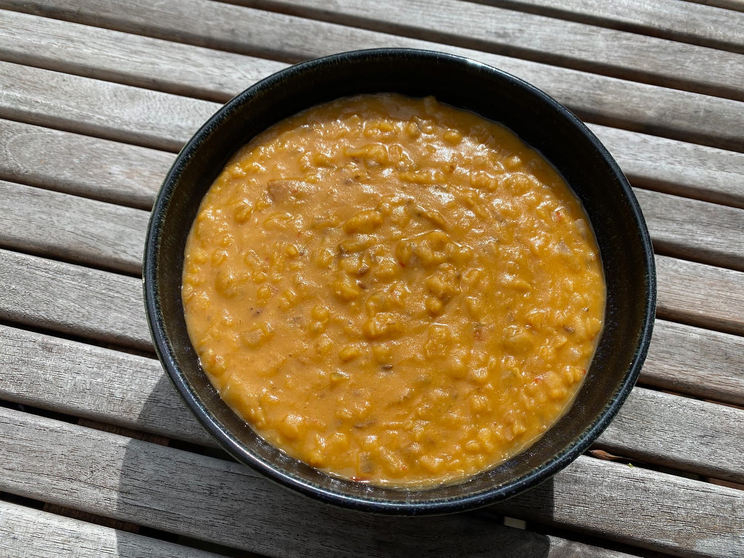 A ceramic bowl of red lentil soup on slated wooden table.