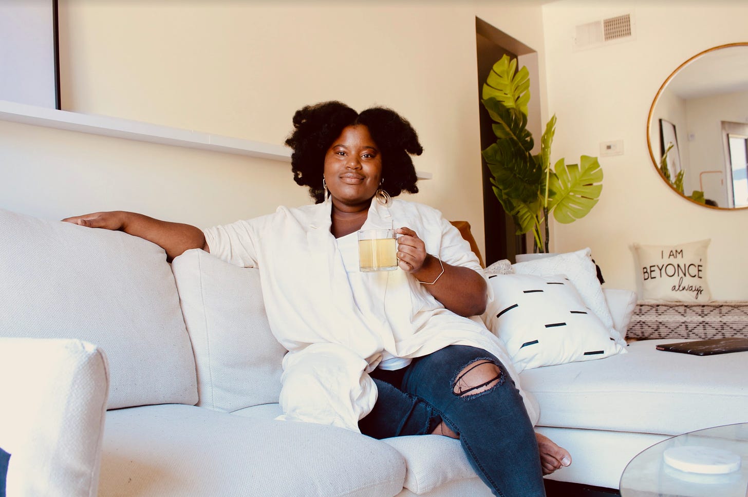 Portrait of Jayde Powell sitting on a white couch drinking tea