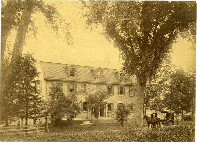 yellowed 19th century photo of stone house with trees in front. Man and woman in buggy