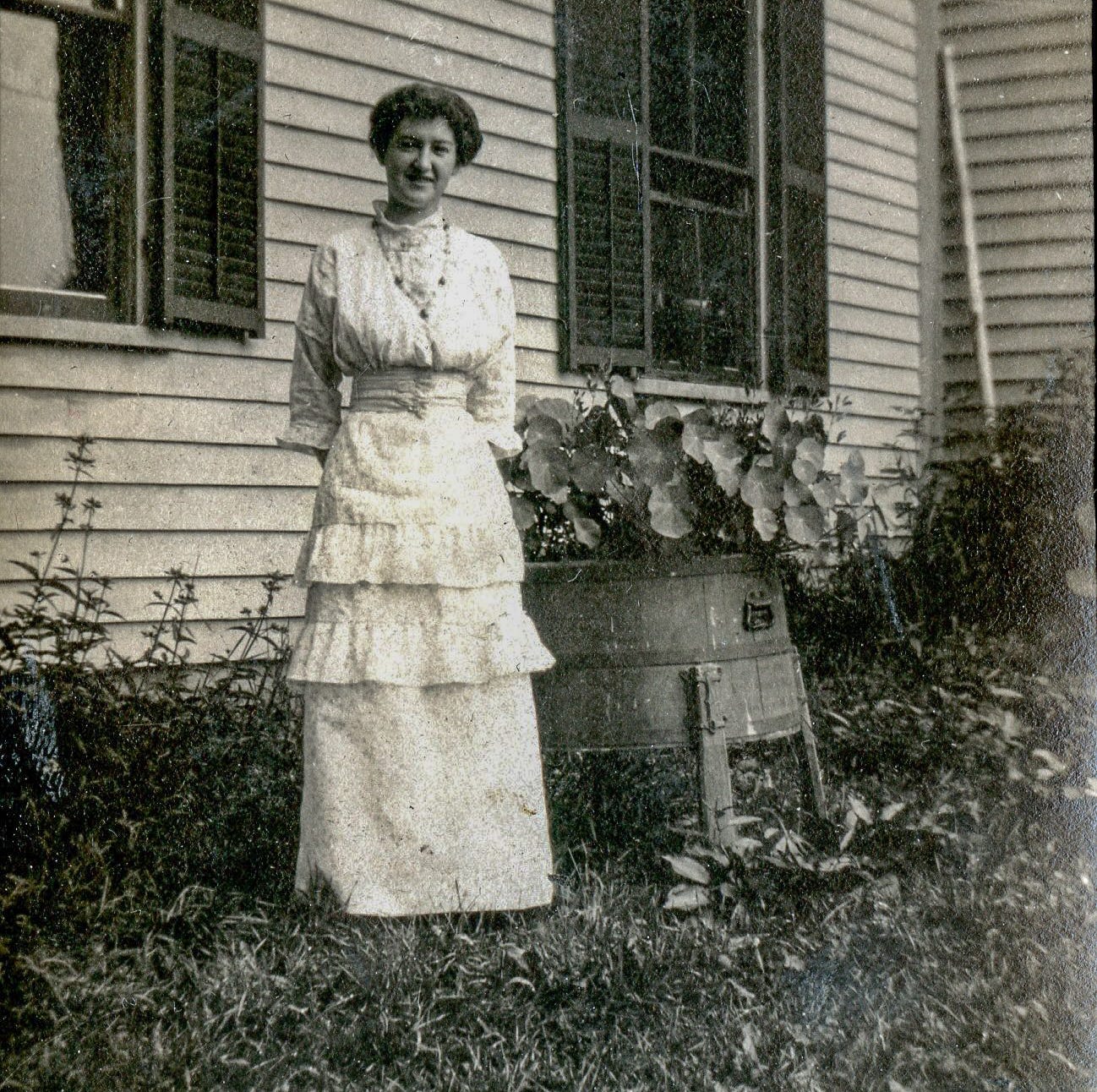 Woman standing outside next to planter with vine