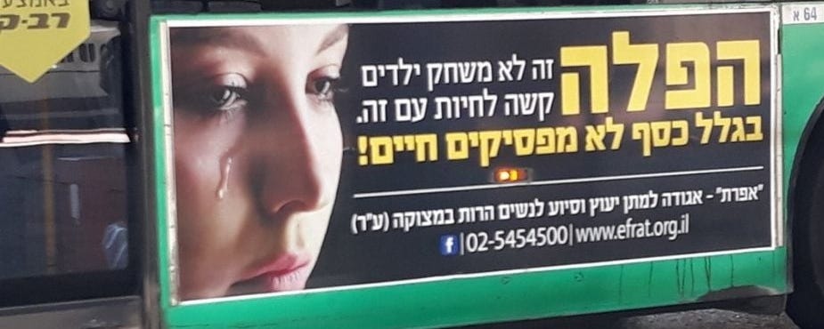 Green bus with an ad on the side, photo of a young woman crying, and text that reads (in Hebrew): “Abortion is not child’s play. It is hard to live with it. You don’t end a life because of money” [Signed], Efrat, the organization giving advice and assistance to pregnant women in crisis. 