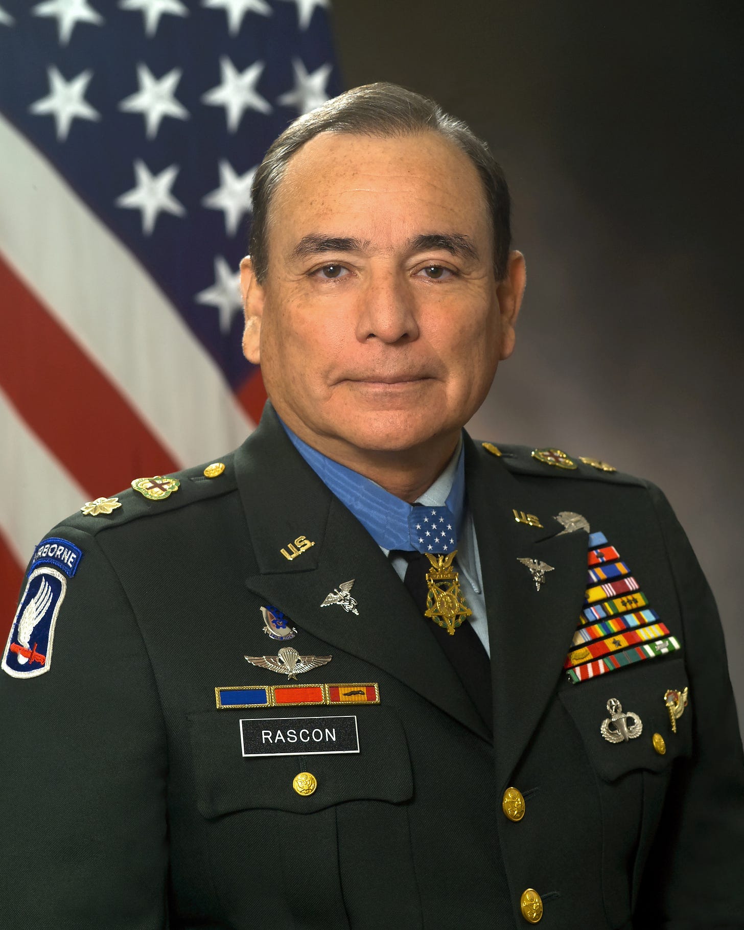 Alfred Rascon, in uniform, wearing his Medal of Honor.  An American flag appears in the background.
