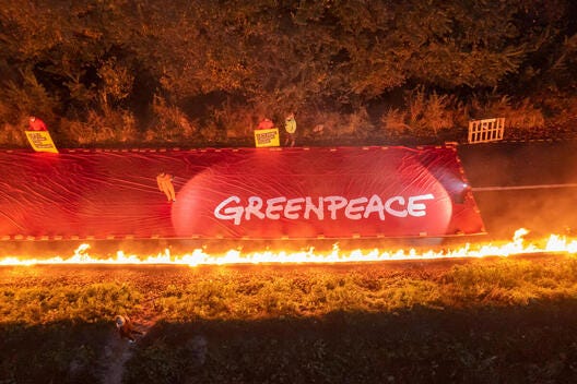 Aerial shot of a symbolic line of fire and a massive Greenpeeace banner drawn between the village of Lützerath and the Garzweiler opencast lignite mine in Germany.
