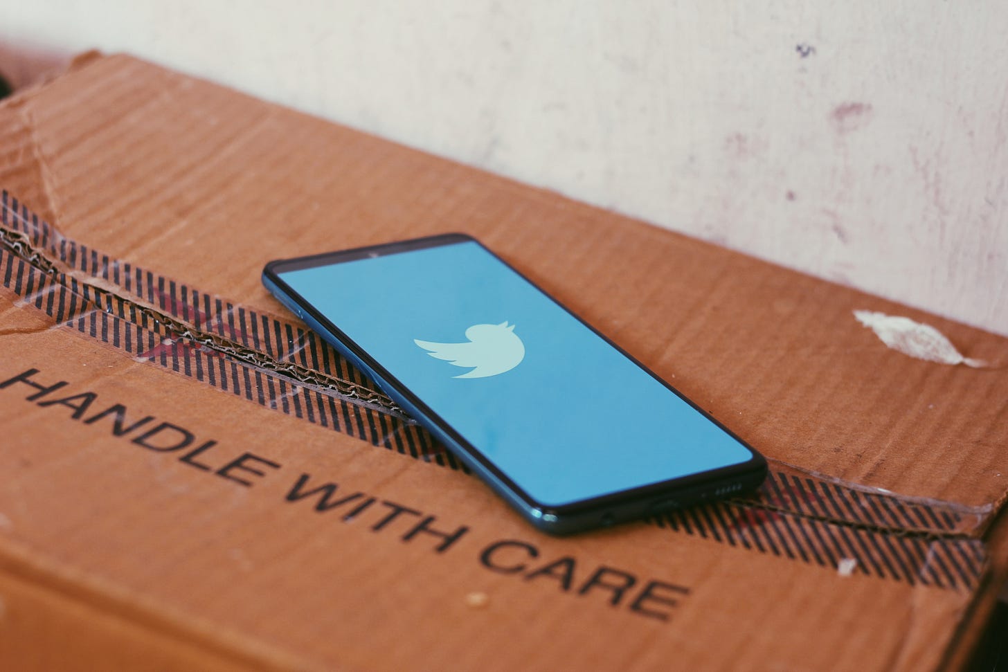 Photo of Twitter on a smartphone on top of a box that reads "handle with care." (Ravi Sharma / Unsplash)