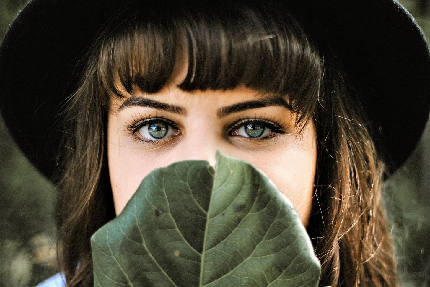 girl with dark hair wearing black hat covering face from the nose down with large green leaf girl with dark hair wearing black hat covering face from the nose down with large green leaf