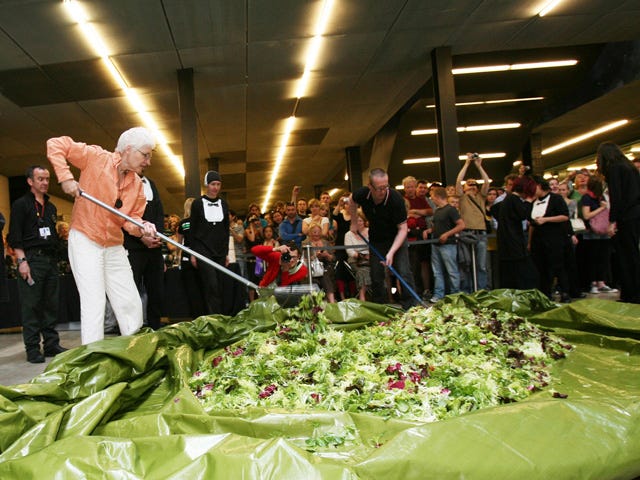 Surrounded by onlookers artist Alison Knowles rakes a giant salad on a tarp