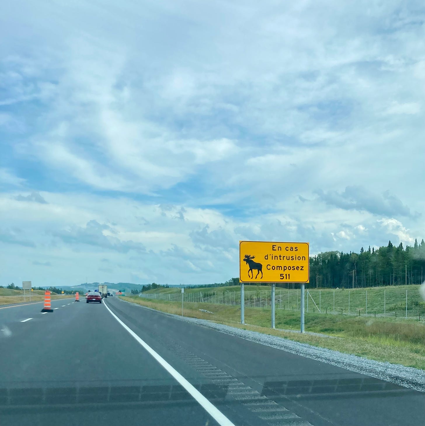 A highway with a large yellow sign on the right with a picture of a moose. The sign reads "En cas d'intrusion Composez 511"