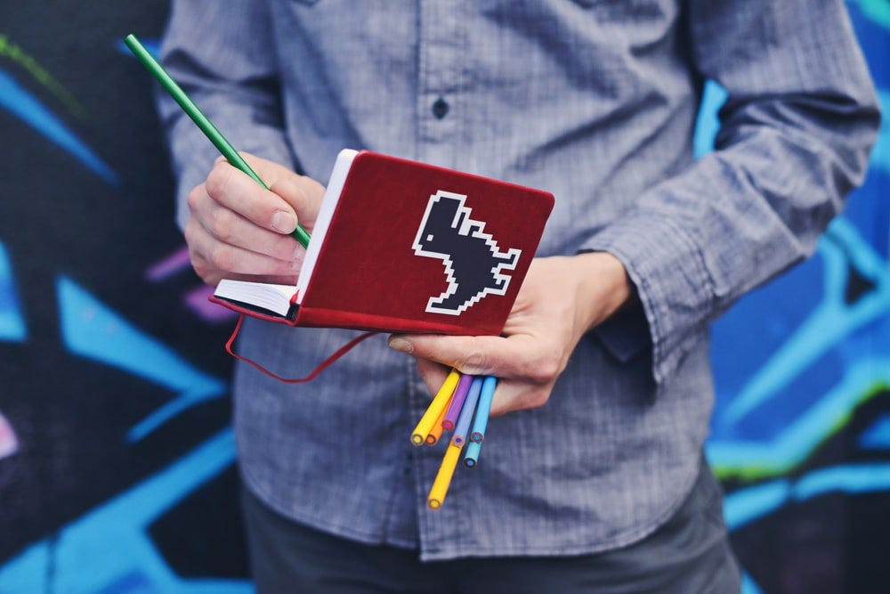 person in blue dress shirt holding red book and colored pens