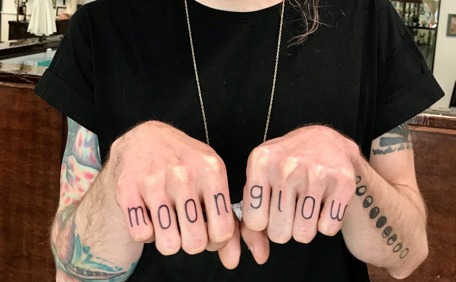 Emme wears a black t-shirt, with her hands in front. MOONGLOW written on her knuckles, freshly tattooed