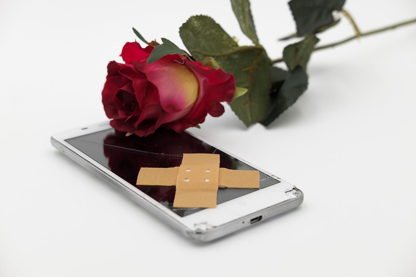 immagine di un cellulare con lo schermo rotto e una rosa sopra