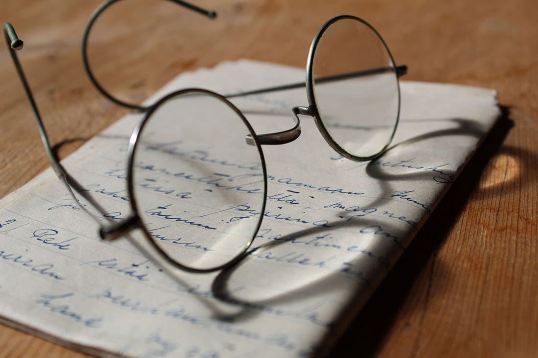 Foto colorida de uma armação redonda de óculos de grau sobre um papel com escrita delicada.