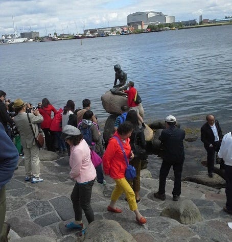 The Little Mermaid statue in Cophenhagen surrounded by crowds.