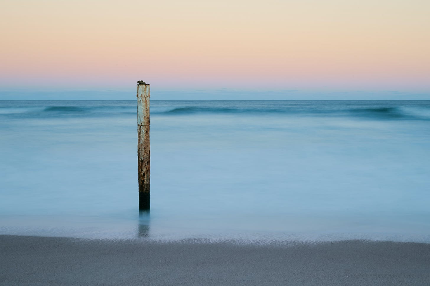 pole sticking out of the sand and water on a beach