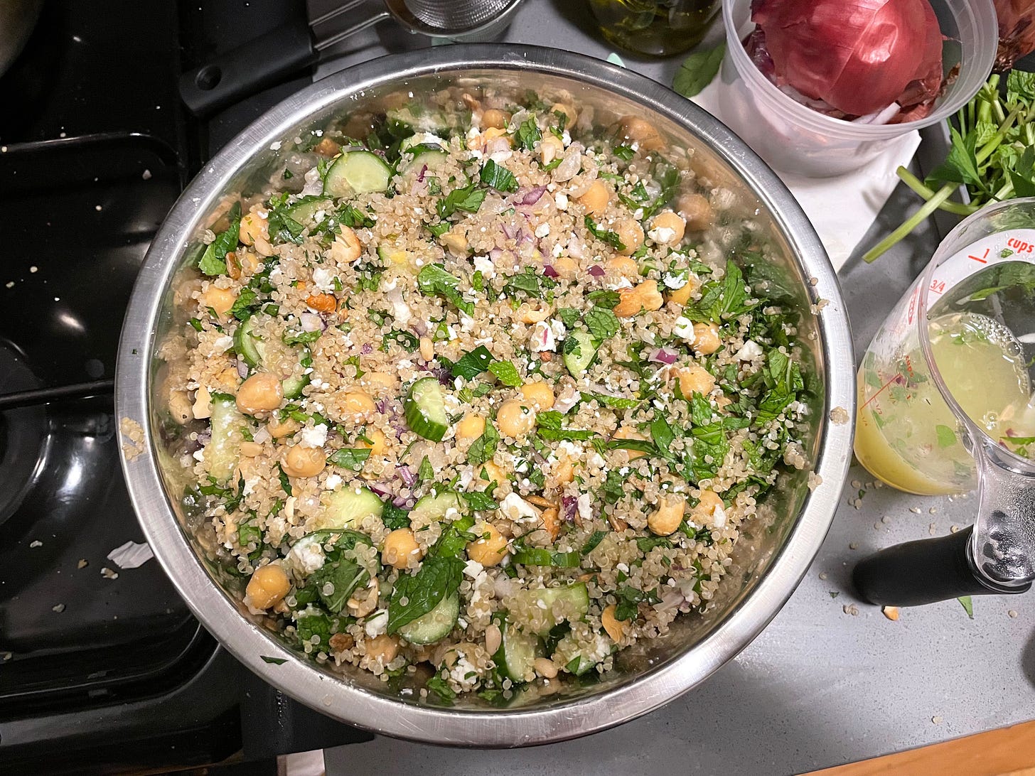 quinoa salad with cucumbers, chickpeas, red onion, nuts, herbs, and feta with measuring cup of lemon juice nearby
