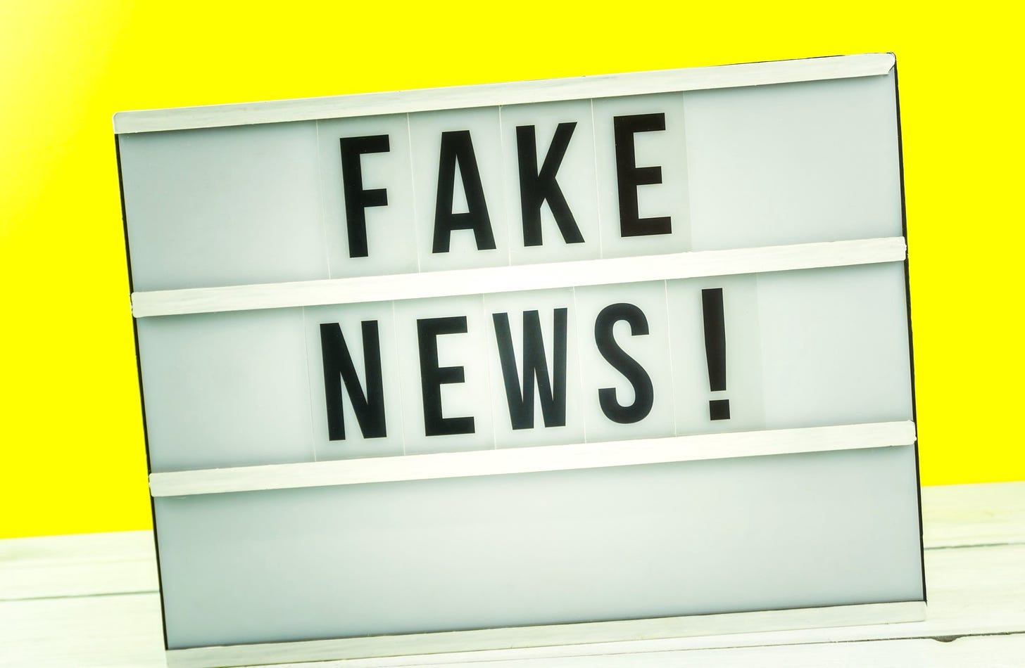 A “fake news” sign sits against a wall of yellow.