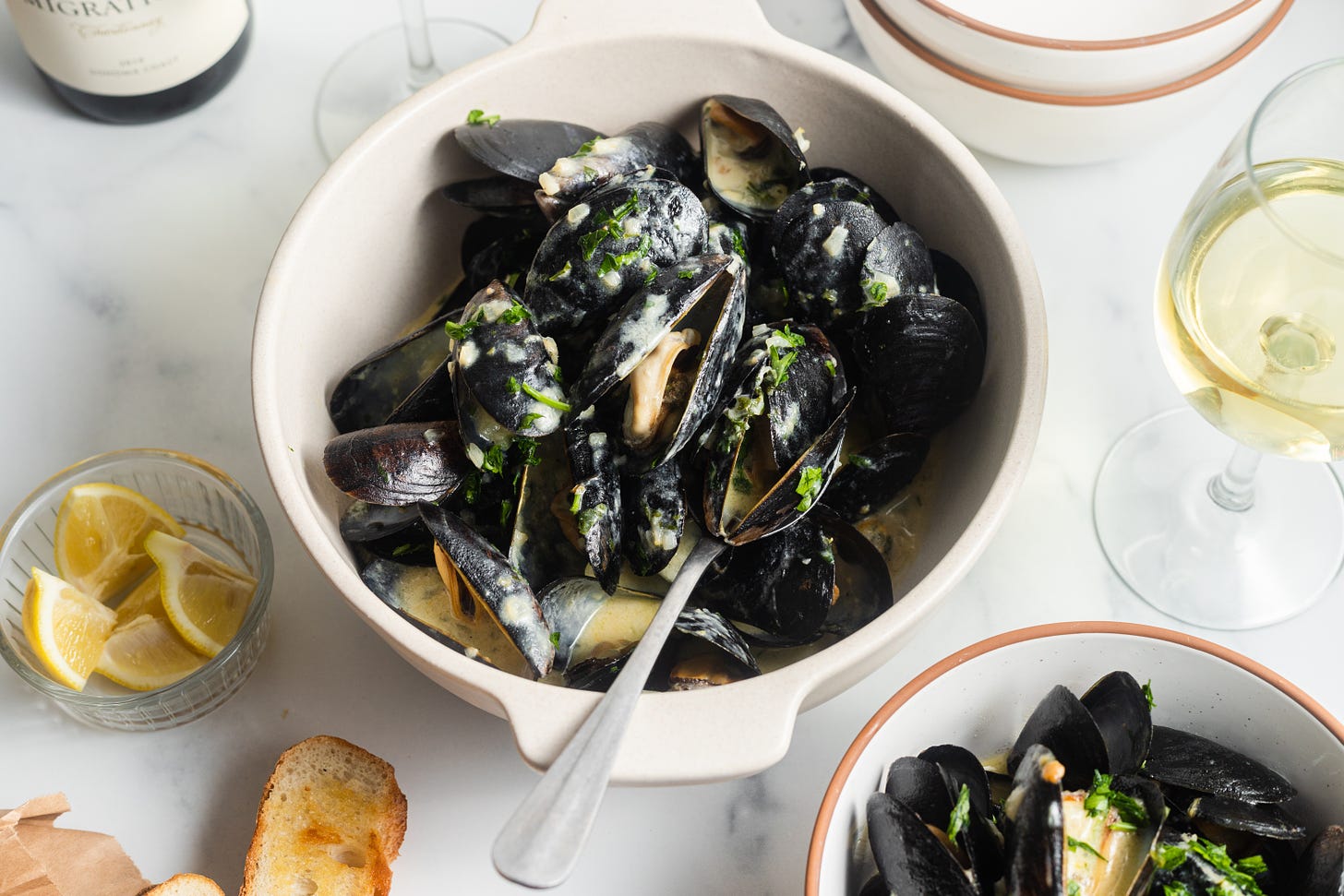 a creamy bowl of mussels with lemon and garlic and a glass of white wine