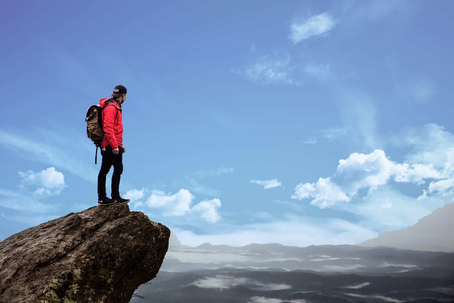 A hiker wearing a red jacket looking over at mountains.