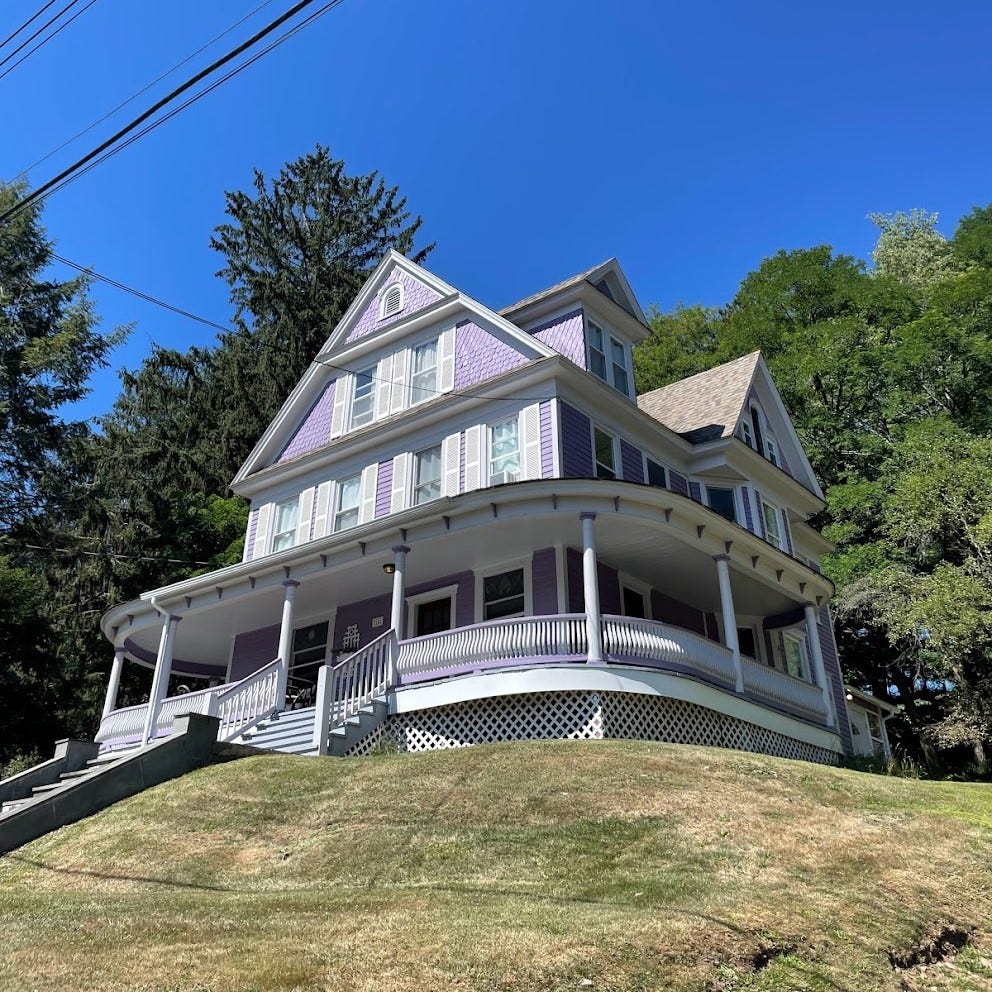 A three story house painted purple with white details, surrounded by nature