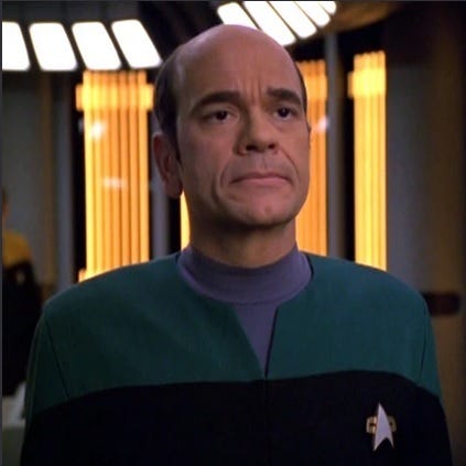 This image shows Star Trek: Voyager's Doctor (Robert Picardo), a sentient hologram, standing near the U.S.S. Voyager's surgical bay (inside the ship's Sickbay).