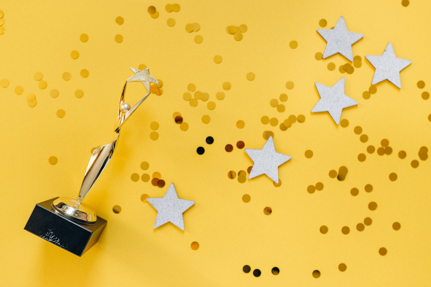 Gold trophy against yellow background with four stars and gold confetti.