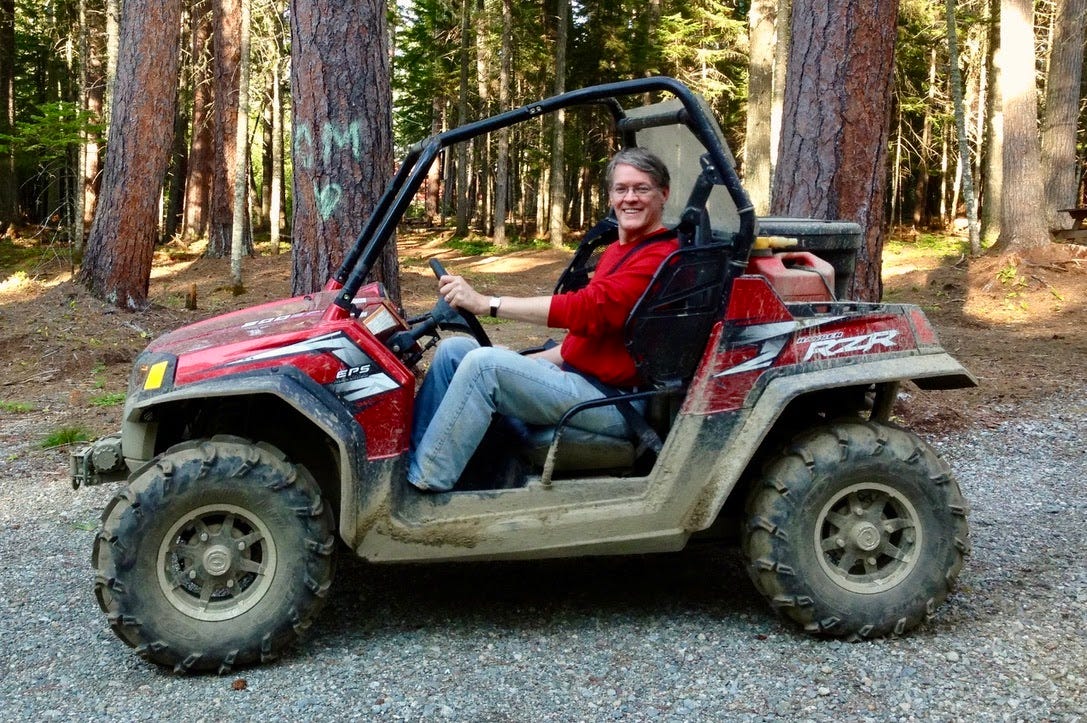 Smiling white man on red ATV in the woods
