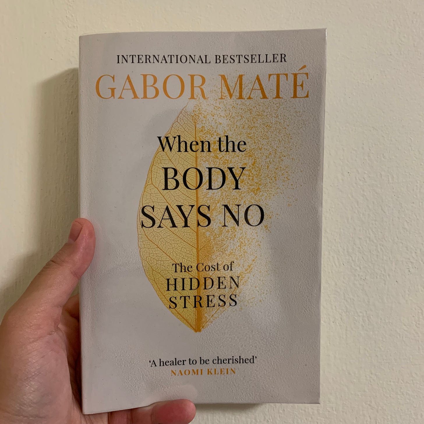Picture of a left hand holding a book titled "When the body says no: The cost of hidden stress" by Gabor Maté