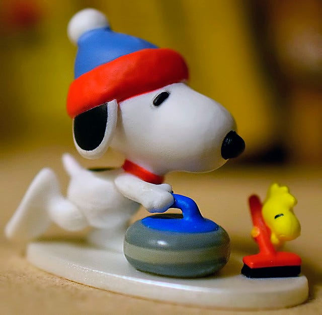 A decoration of Snoopy throwing a curling rock with Woodstock sweeping
