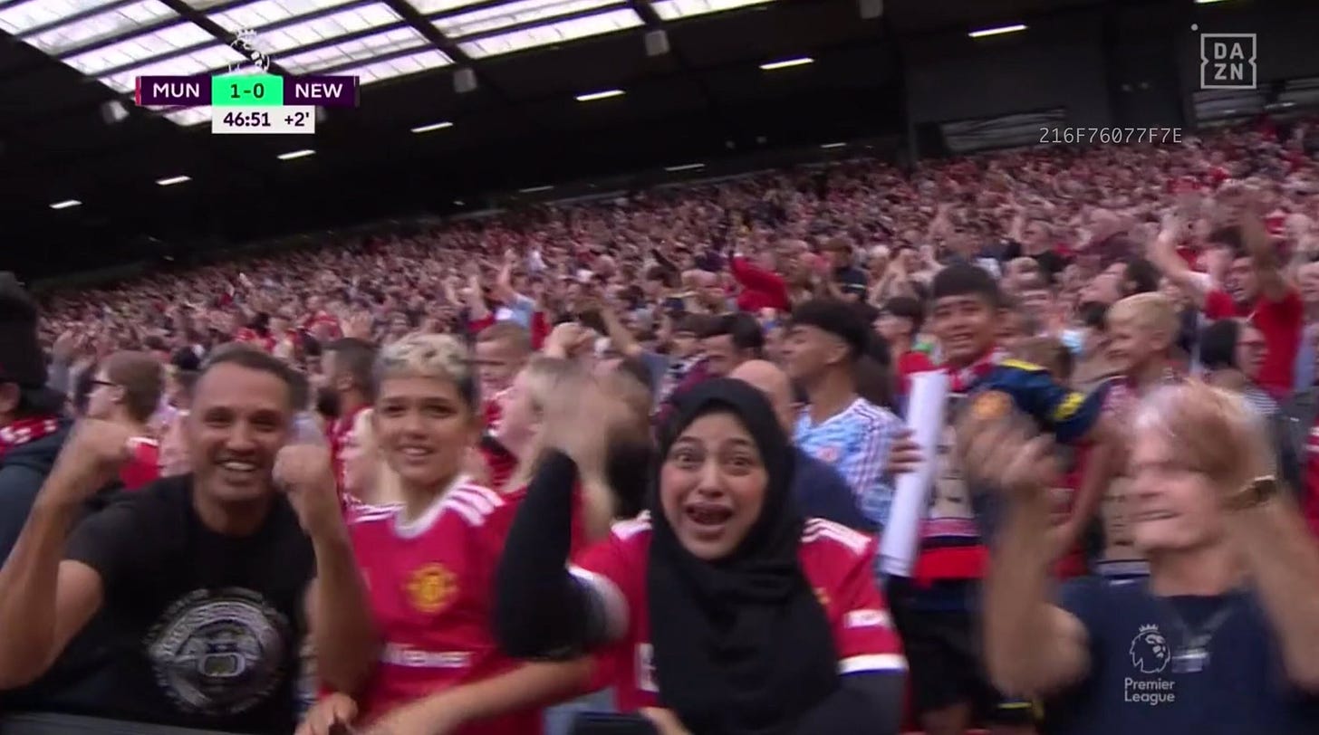 Football stadium full of supporters. At the front visible is a woman wearing a black headscarf waving her arm in celebration