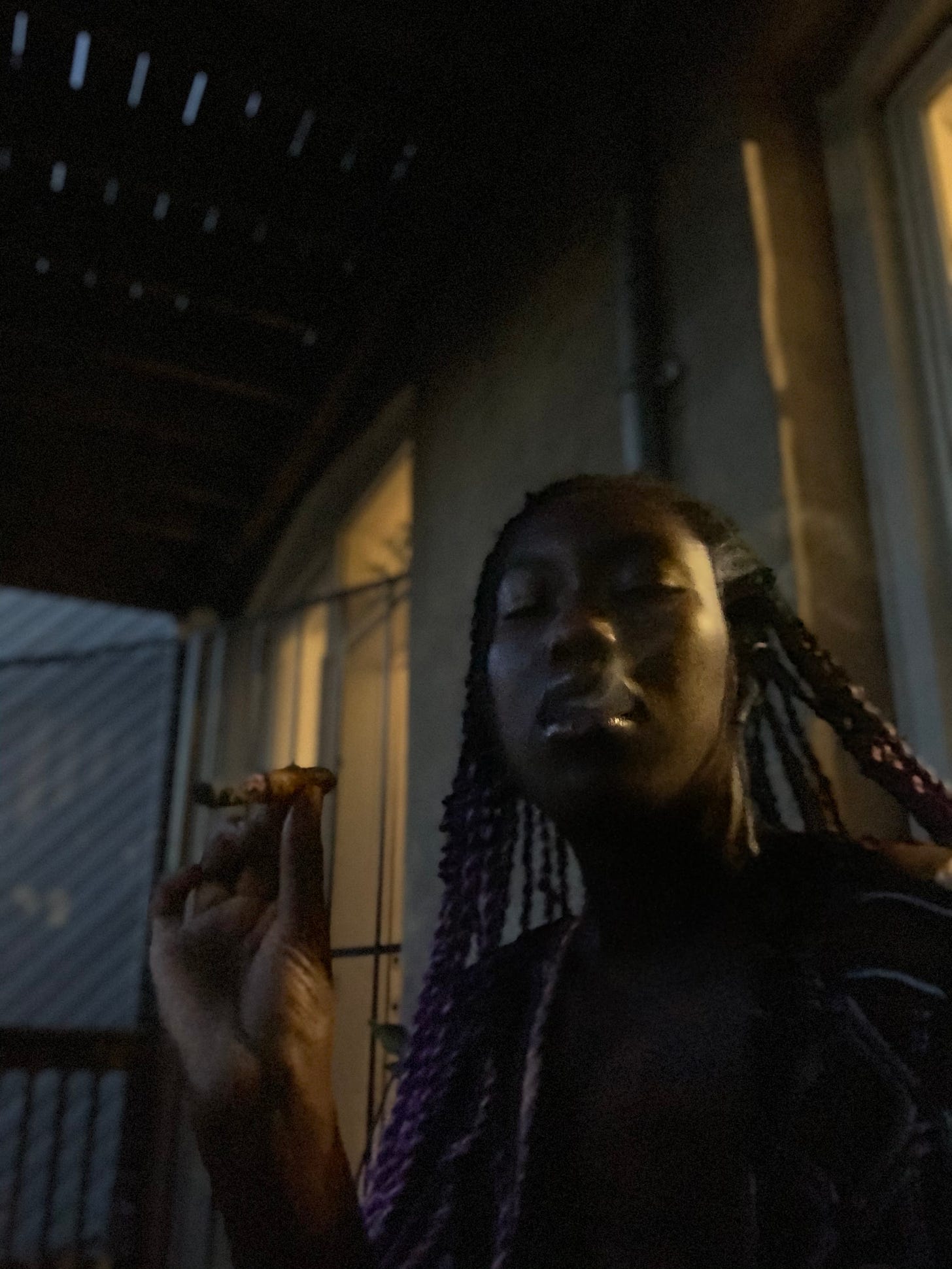 selfie of Ismatu smoking a cigar in the late Chicago evening backlit by her apartment 