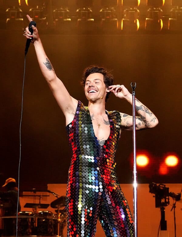 Harry Styles wearing a silver sequined bodysuit while performing onstage.