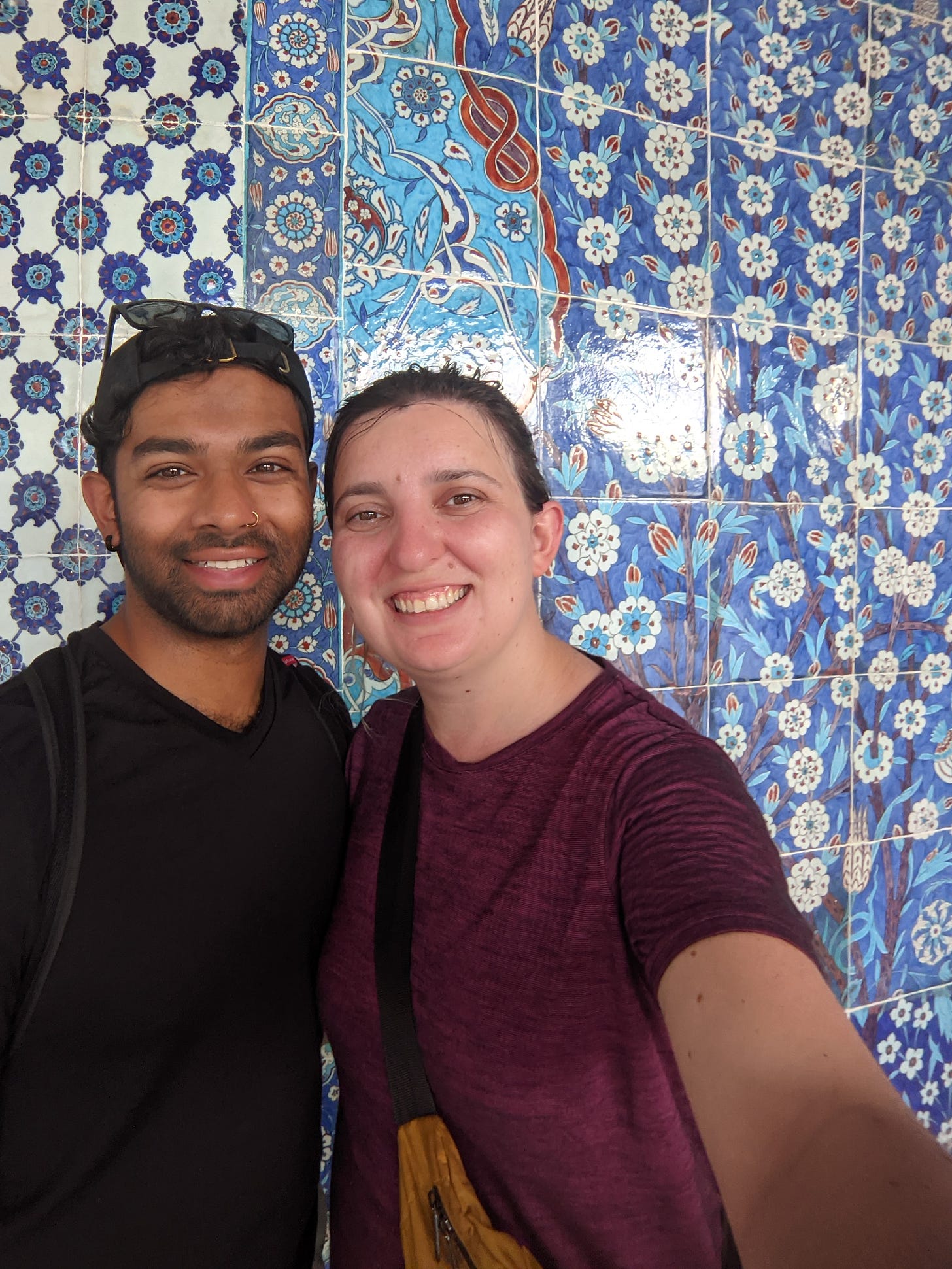 Iulia and Aseef taking a picture in front of blue tiling, featuring red accents, and flower patterns