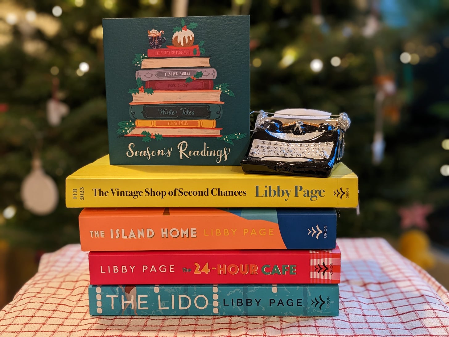 A stack of Libby Page's books with a Christmas card reading Season's Readings, and a typewriter ornament. 