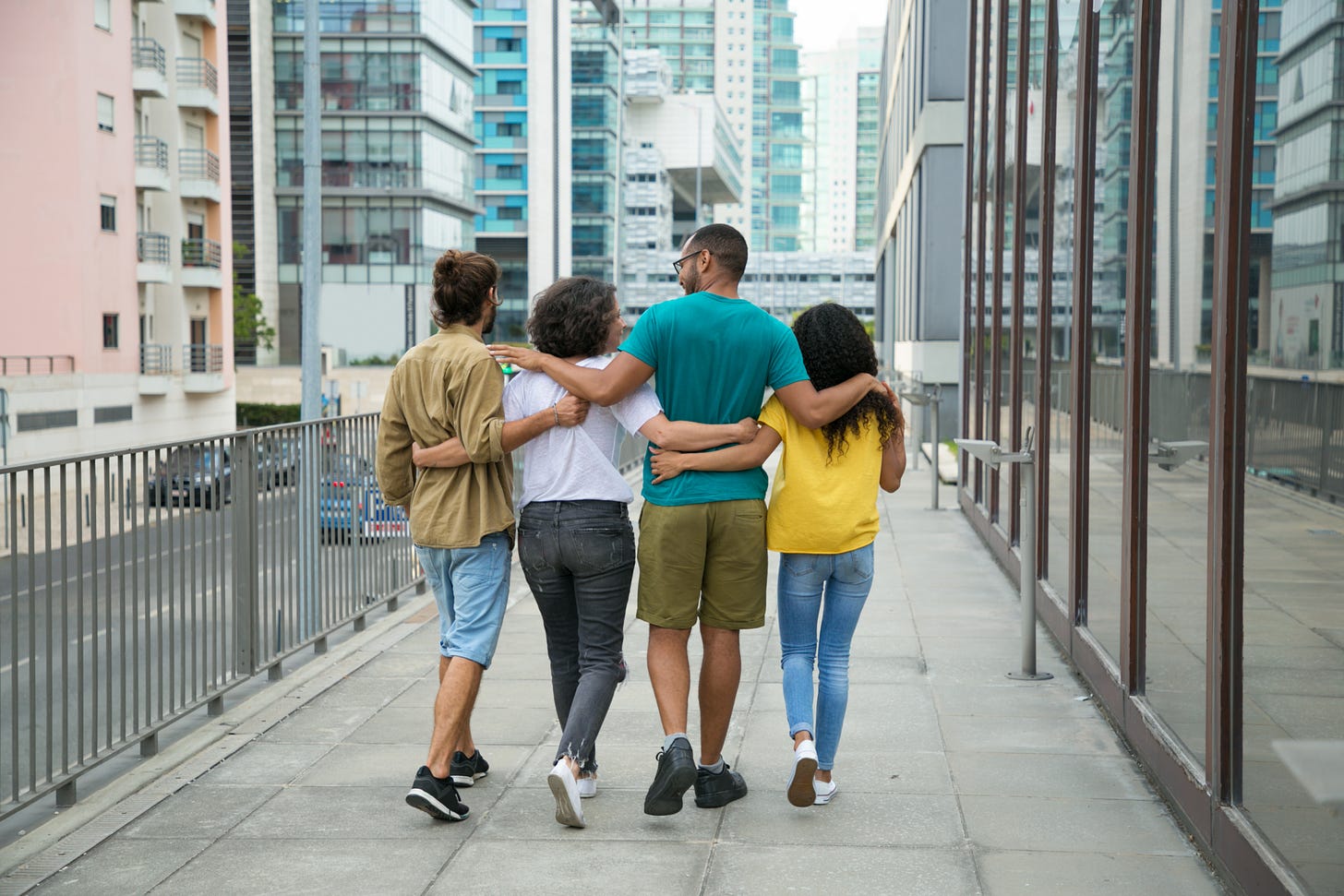 A group of four people are walking down the sidewalk in a big city scene. You can only see them from the back, and they all have their arms around each other. Looks like a guy with a pony tail, then a lady with a white blouse and short hair, then a tall guy with a teal shirt and glasses, and finally a girl with long black hair and a yellow shirt. They look polyamorous as fuck which is why I chose this image