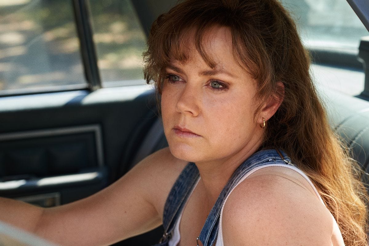 Amy Adams sits in a car, wearing overalls.