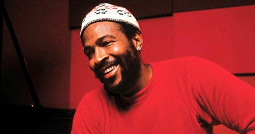 This image shows Marvin Gaye, dressed in a blood-red T-shirt, smiling as he sits in front of a red background.