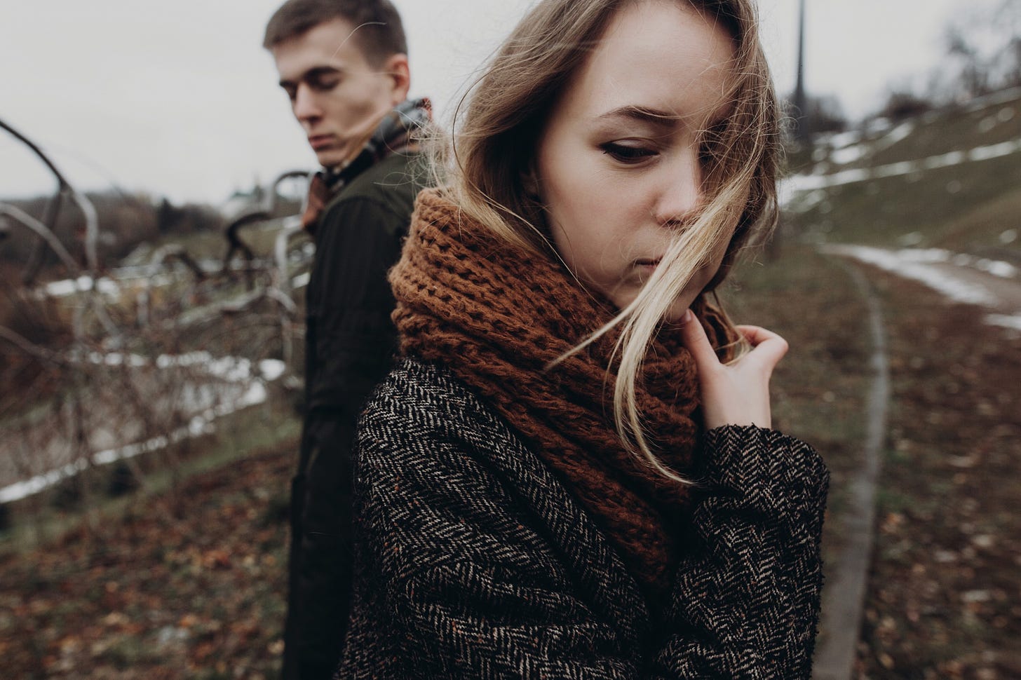 A moody couple look at one another over their shoulders.