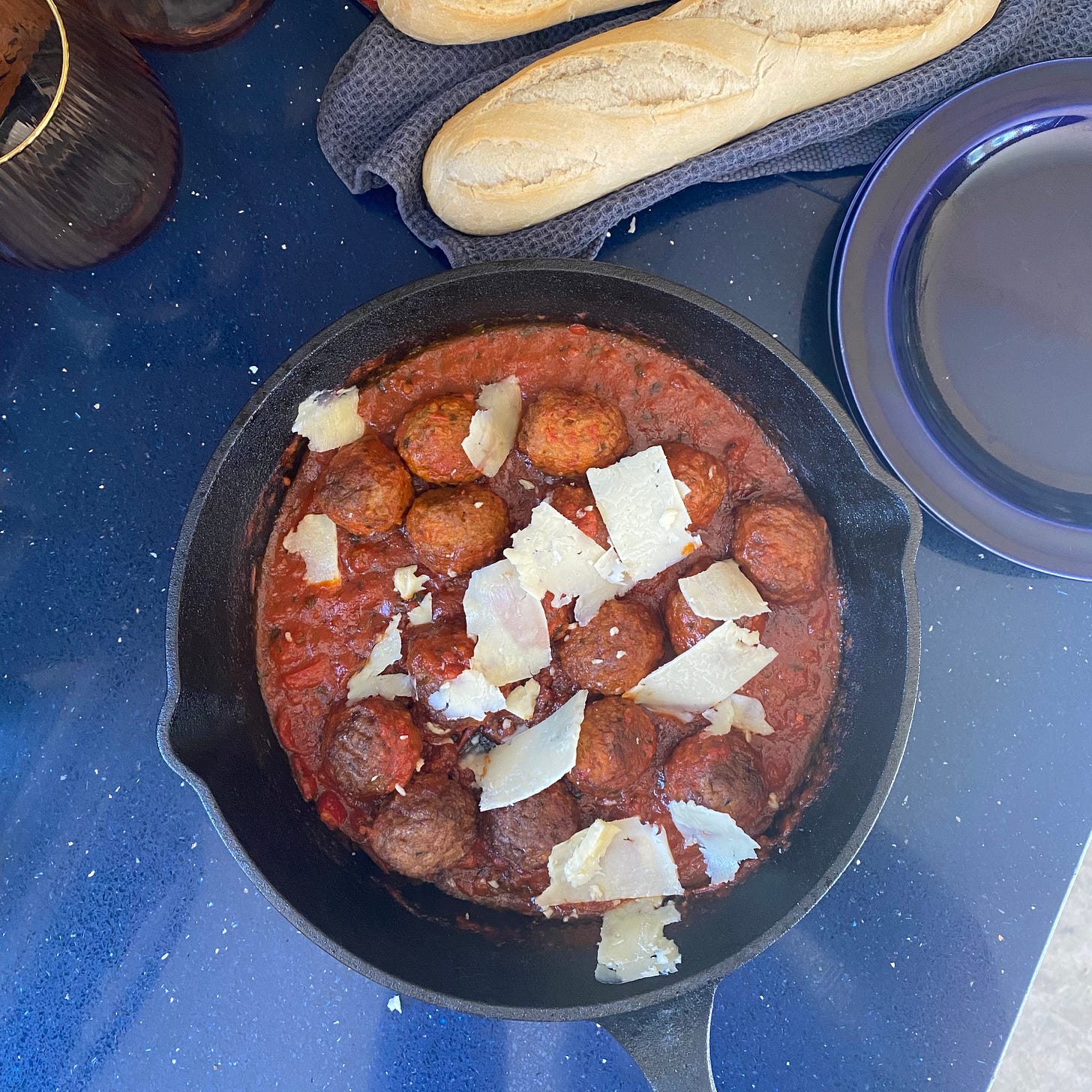 Skillet pan of meatballs in tomato sauce, with two baguettes above and blue plates to the side.