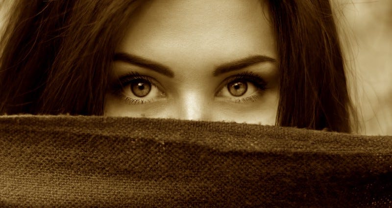 Sepia photo of woman's eyes with bottom of her face shielded by outstretched cloth.