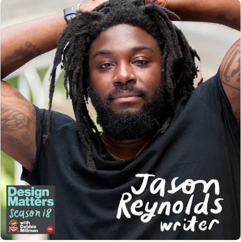 Close up of Jason Reynolds, Black man with dreadlocks, full beard, deep brown skin. Tatooed arms are up over his head, elbows bent.