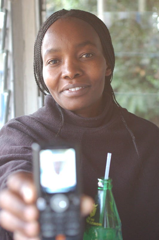 black woman with long braids holding a cell phone toward the camera