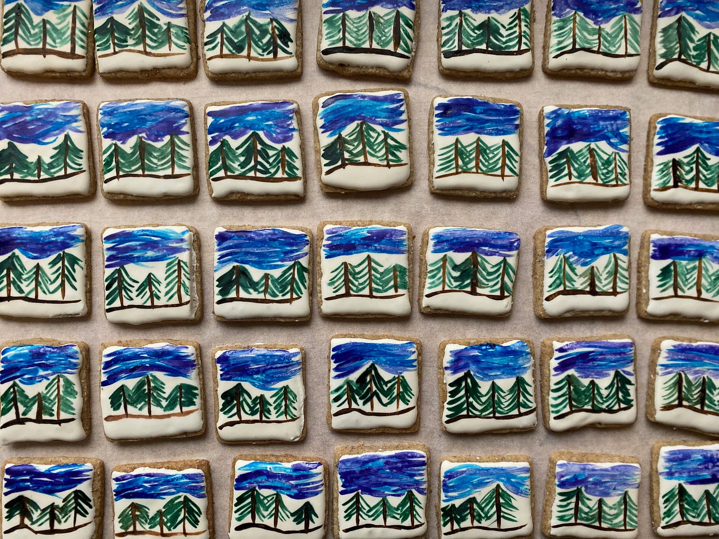 A closeup of several dozen small square cardamom rye cookies, lined up in rows. The cookies are frosted white, and have small painted scenes on them: three evergreen trees under a blue sky.
