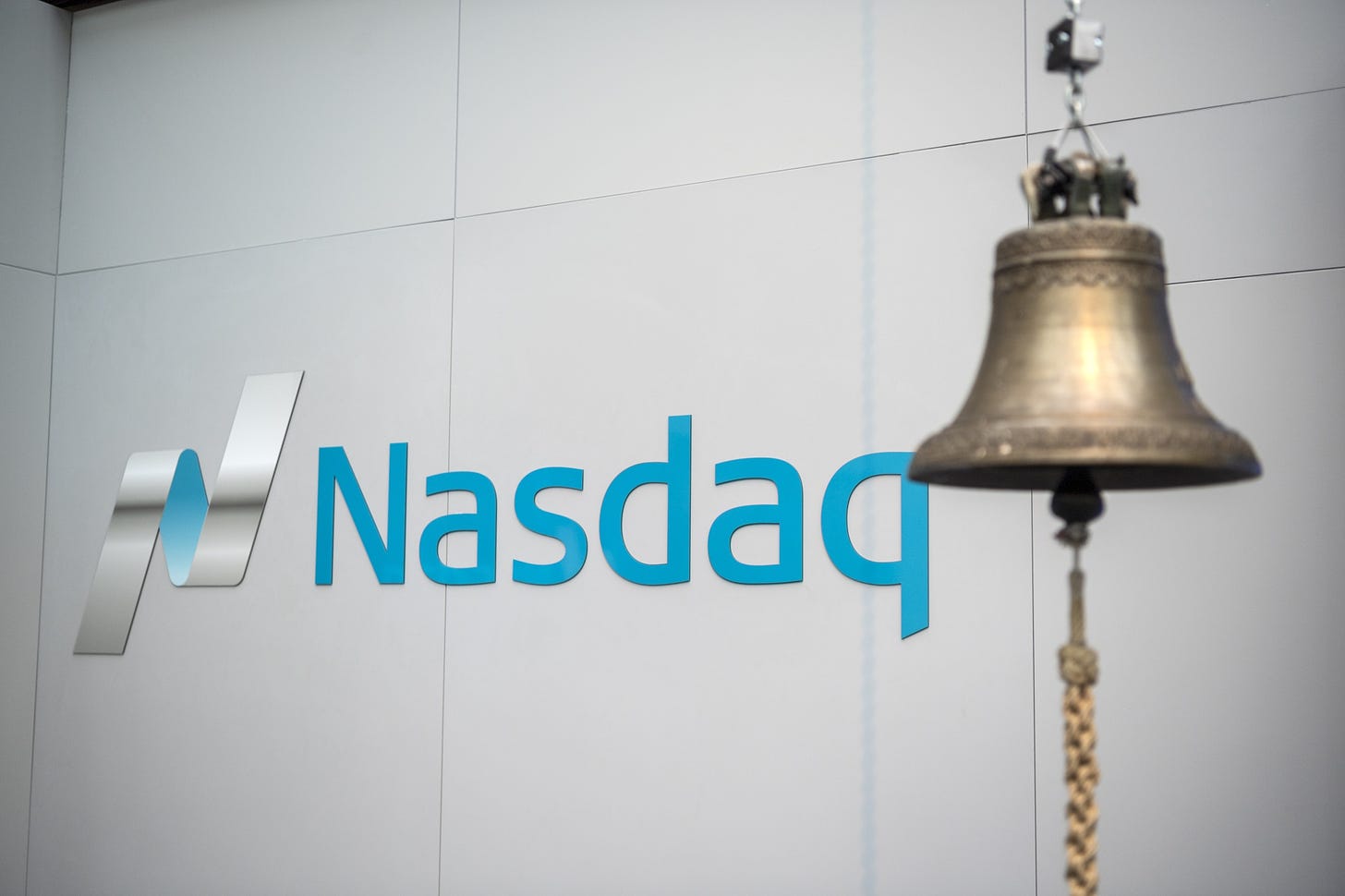 A trading bell hangs in front of Nasdaq signage.&nbsp;