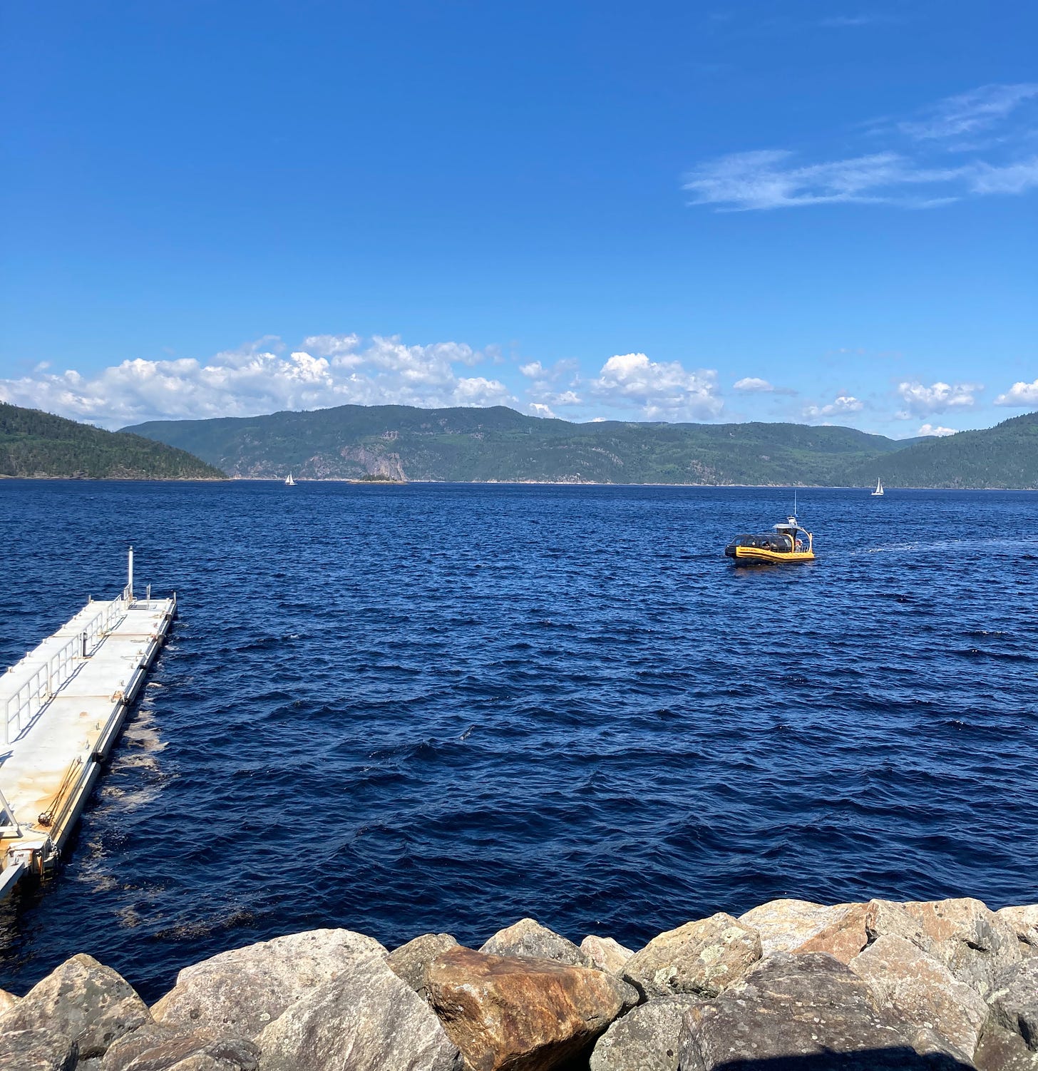 A yellow boat arriving to a floating dock. The water is deep blue, and there are green hills in the background.