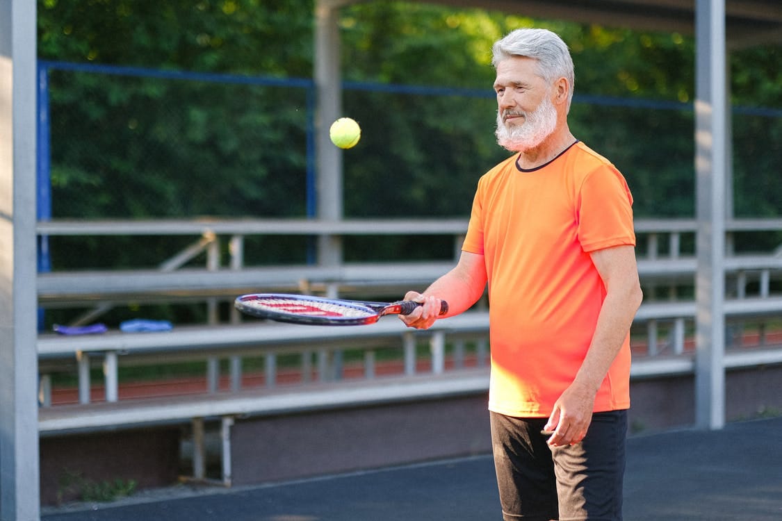 Cheerful aged sportsman playing tennis on tennis court