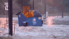 An animated gif of a garbage dumpster in flames floating down a flooded street.
